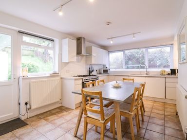 A kitchen with a dining table and chairs next to white cabinets and windows at The Bridge House Southwold