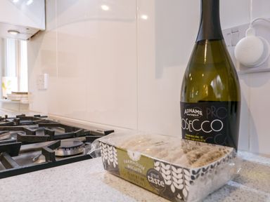 A kitchen countertop with a bottle of prosecco and a packet of farmhouse biscuits next to a gas stovetop at The Bridge House Southwold