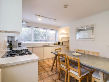 A kitchen with a long dining table and wooden chairs next to countertop and sink at The Bridge House Southwold