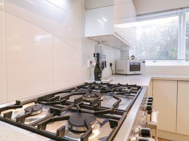 A kitchen countertop with a gas stove microwave knife set and a bottle at The Bridge House Southwold