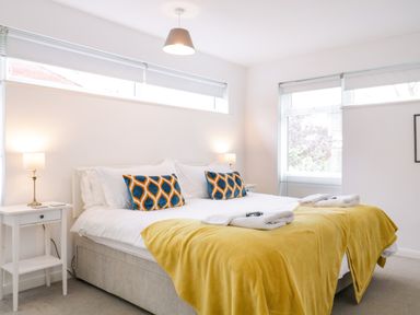 A bedroom with a bed with yellow blankets and patterned pillows and two bedside tables with lamps at The Bridge House Southwold