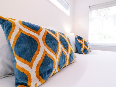 Two decorative pillows with blue orange and white geometric pattern on a white bed near windows at The Bridge House Southwold