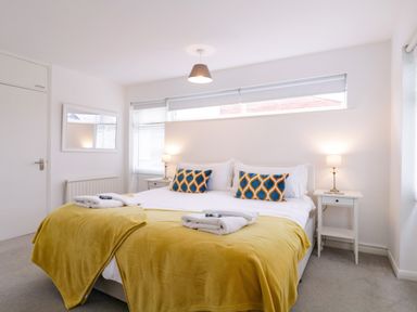 A bedroom with a double bed yellow blankets patterned pillows bedside tables lamps and a wall mirror at The Bridge House Southwold
