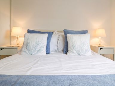 A bed with white and blue pillows beside two bedside tables with lamps at The Bridge House Southwold