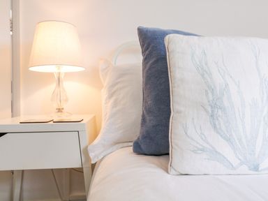A bedside table with a lamp next to a bed with stacked pillows at The Bridge House Southwold