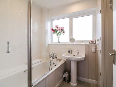 A bathroom with a bathtub a pedestal sink a window with flowers on the sill and a small trash bin at The Bridge House Southwold