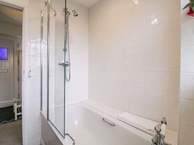 A bathroom with a bathtub with a glass shower screen and a folded towel on the tub edge at The Bridge House Southwold