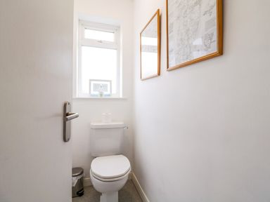 A small bathroom with a toilet a window above and framed pictures on the wall at The Bridge House Southwold