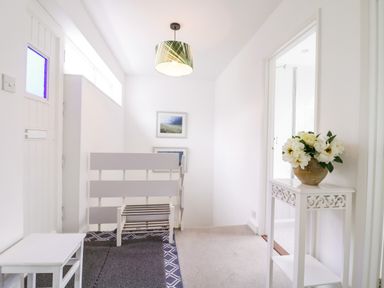 A hallway with a white door a small white table and a white decorative stand with flowers on it at The Bridge House Southwold