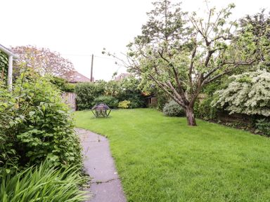 A garden with a tree and outdoor table with chairs on grass at The Bridge House Southwold