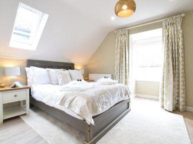 A bedroom with a gray bed frame white bedding and pillows bedside tables with lamps and patterned curtains at The Red Brick House in Aldeburgh