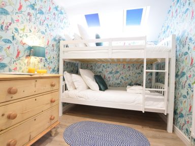 A bedroom with a wooden dresser and white bunk beds with pillows and a round blue rug at The Red Brick House Aldeburgh