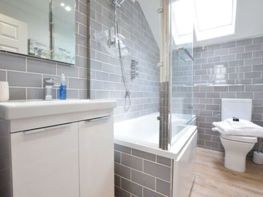 A bathroom with a white sink cabinet bathtub with shower and a toilet with towels at The Red Brick House Aldeburgh