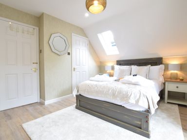 A bedroom with a bed, bedside tables, lamps, a skylight window, two doors, a mirror, and a rug at The Red Brick House in Aldeburgh