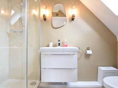 A bathroom with a white sink and vanity under a mirror flanked by two lights next to a glass-enclosed shower at The Red Brick House Aldeburgh