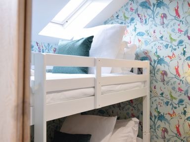 A bunk bed with white bedding and turquoise pillows by a skylight window in a room with bird patterned wallpaper at The Red Brick House Aldeburgh