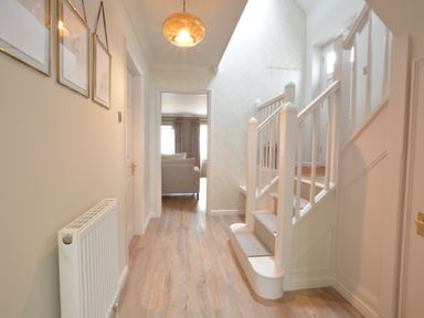 A hallway with wooden flooring white stairs and a radiator at The Red Brick House in Aldeburgh