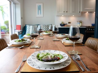 A dining table set with plates of salad and glasses of red wine in a kitchen at The Red Brick House in Aldeburgh