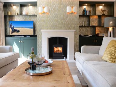 A living room with a fireplace televisions and wine glasses on a wooden table at The Red Brick House Aldeburgh