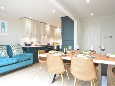 A kitchen dining area with a wooden table set for six with wine glasses and a teal sofa with patterned pillows at The Red Brick House in Aldeburgh