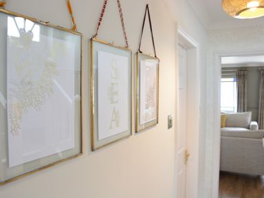A hallway with three framed pictures hanging on the wall and a view of a living room with a couch at The Red Brick House in Aldeburgh