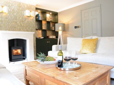 A living room with a wooden coffee table holding a wine bottle and glasses in front of a white sofa with a yellow pillow at The Red Brick House Aldeburgh