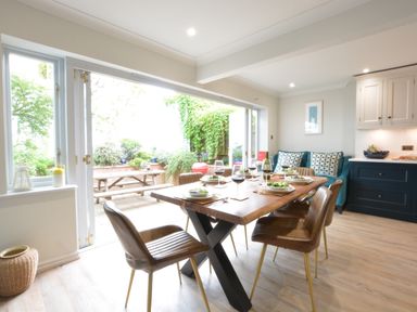 A dining area with a wooden table set for six and chairs next to an open patio door at The Red Brick House Aldeburgh