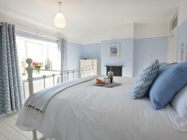 A bedroom with a white bed blue and white pillows blue patterned curtains and a tray with breakfast on the bed at Somewhere Only We Know in Aldeburgh