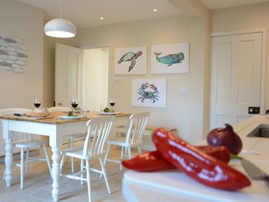 A dining room with a wooden table set with plates and wine glasses and white chairs at Somewhere Only We Know in Aldeburgh