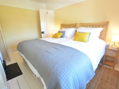 A bedroom with a double bed featuring wooden headboards yellow and gray cushions white bedding a gray quilt bedside tables with lamps and a mug on one at Somewhere Only We Know Aldeburgh