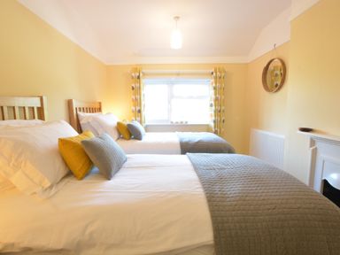 A bedroom with two single beds pillows and blankets near a window with patterned curtains at Somewhere Only We Know in Aldeburgh