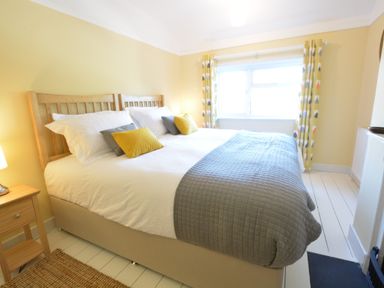 A bedroom with a large bed yellow patterned curtains and a bedside table at Somewhere Only We Know Aldeburgh