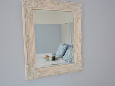 A mirror with an ornate frame reflecting a bed with blue patterned pillows and breakfast items at Somewhere Only We Know in Aldeburgh