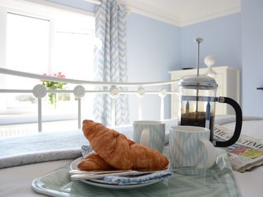 A breakfast tray with croissants coffee cups and a French press on a bed in a bedroom with blue walls at Somewhere Only We Know in Aldeburgh