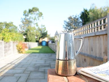 A metal coffee pot on a brick wall next to a folded newspaper with a backyard in the background at Somewhere Only We Know Aldeburgh