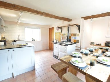 A kitchen with a wooden dining table set with bowls of salad and glasses at The White House with Studio in Wortwell