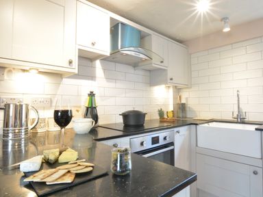 A kitchen with white cabinets black countertops a stove a sink and snacks on the counter at The White House with Studio in Wortwell