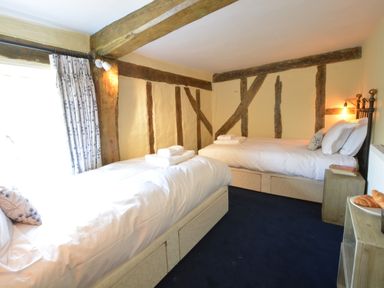 A bedroom with two single beds wooden beams and a window with curtains at The White House with Studio in Wortwell