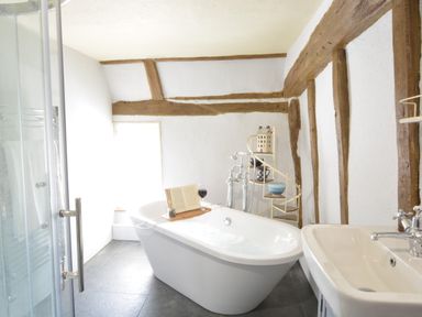 A bathroom with a freestanding bathtub holding a book and glass of wine a sink and exposed wooden beams on the walls at The White House with Studio in Wortwell