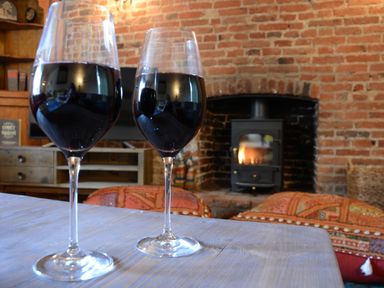 Two glasses of red wine on a wooden table with a fireplace and brick wall in the background at The White House with Studio in Wortwell