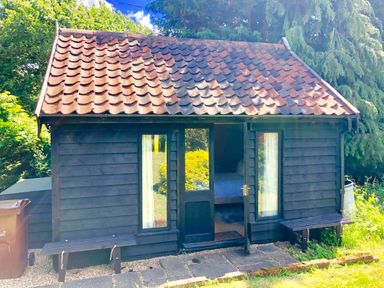A small black wooden cabin with two windows and benches on each side of the door at The White House with Studio in Wortwell