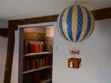 A model hot air balloon hanging in front of a bookshelf with books at The White House with Studio in Wortwell