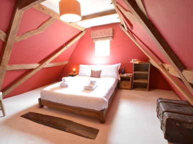 A bedroom with a double bed white bedding wooden beams red walls and trunks at The White House with Studio in Wortwell