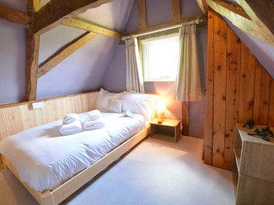 A bedroom with a single bed, white bedding, a bedside table with a lamp, a window with curtains, wooden beams and wood paneling on the walls at The White House with Studio in Wortwell