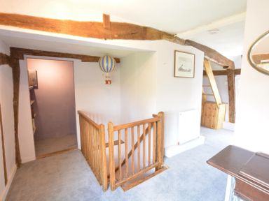 A hallway with wooden handrails around stairs wooden beams on walls and ceiling a small bookshelf and a framed picture at The White House with Studio in Wortwell