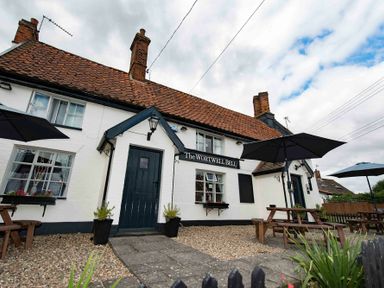 A white building with a brown tiled roof and black door with outdoor wooden tables and umbrellas at The White House with Studio in Wortwell