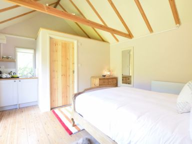 A bedroom with a wooden bed a chest of drawers a mirror and a small kitchen area at The White House with Studio in Wortwell