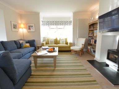 A living room with blue and yellow sofas a striped rug a coffee table a white armchair a bookshelf and a television at Mellows Thorpeness in Thorpeness