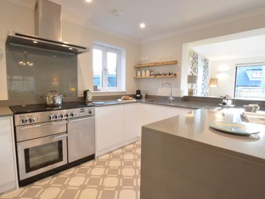 A kitchen with a stove dishwasher sink countertop and shelves with cups and glasses at Mellows Thorpeness in Thorpeness