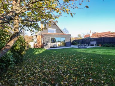 A backyard with a lawn table and benches and a two-story house with large glass doors at Mellows Thorpeness in Thorpeness